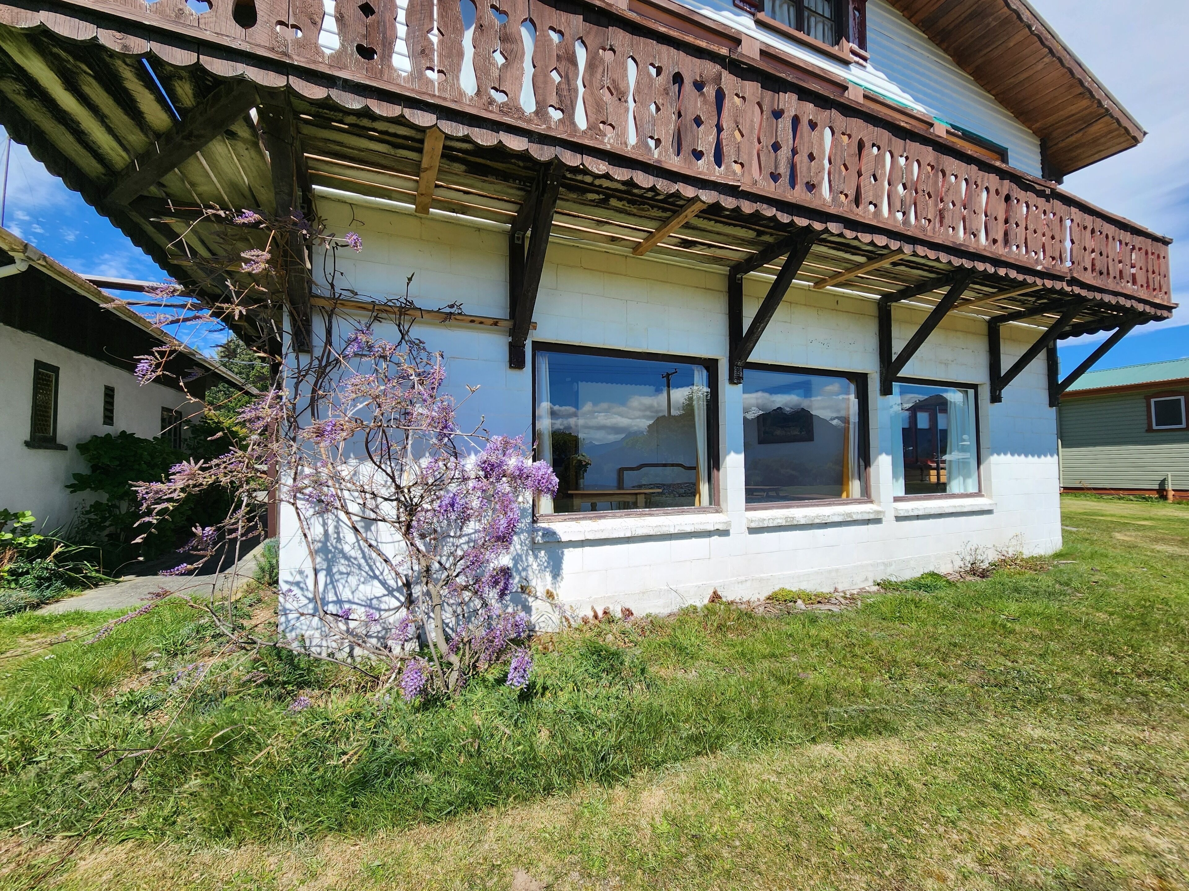 A two-story building with a balcony, large windows, and a garden with purple flowers.