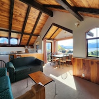 Un interior acogedor con techo de madera, una zona de comedor con mesa y sillas, un sofá y una cocina con fregadero y armarios.