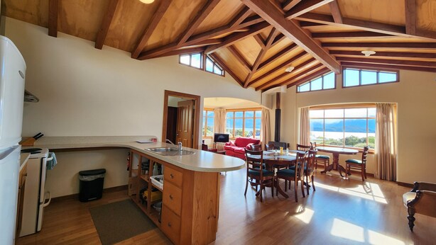 A spacious kitchen with a wooden island, a dining area with a table and chairs, and large windows offering a view. - Manapouri Holiday Park (Manapouri)