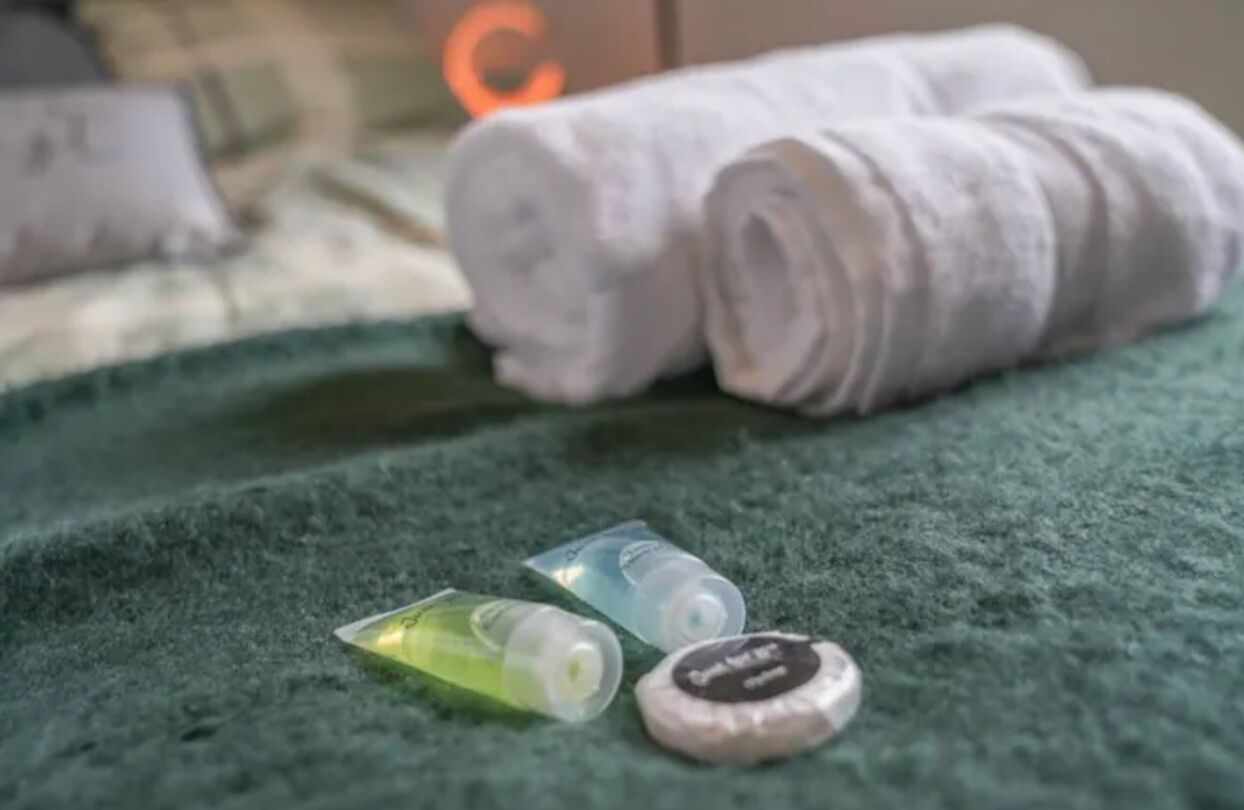 Superficie verde con textura, toallas blancas enrolladas y tres pequeños recipientes.