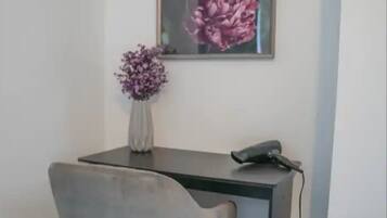 A modern office desk with a grey chair, a vase with purple flowers, and a framed floral painting on the wall.