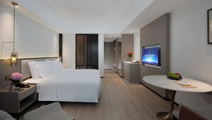 A modern hotel room with a bed, bedside table, lamp, TV, and a small dining area. - Fuqinglong Huatian Holiday Hotel (Shenzhen)