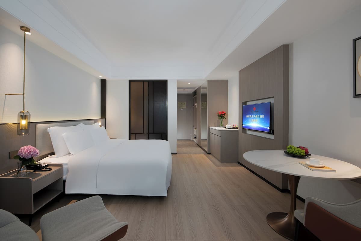 Een moderne hotelkamer met een bed, nachtkastje, lamp, televisie en een eethoekje.