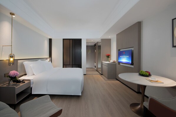 A modern hotel room with a bed, bedside table, lamp, TV, and a small dining area. - Fuqinglong Huatian Holiday Hotel (Shenzhen)