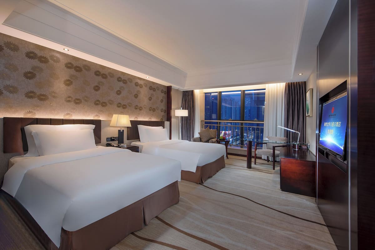 Een hotelkamer met twee bedden, een televisie, een bureau en uitzicht op de stad.