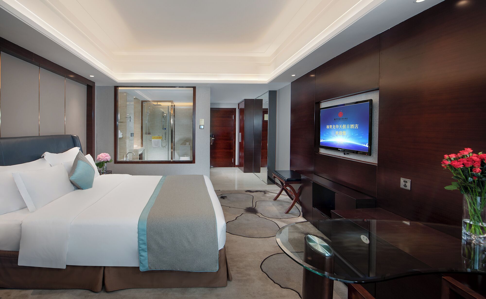 Una habitación de hotel moderna con una cama grande, un televisor montado en la pared y una mesa de centro de vidrio.