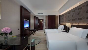 Habitación de hotel con cama, mesitas de noche, televisión y una mesa de vidrio con un florero.