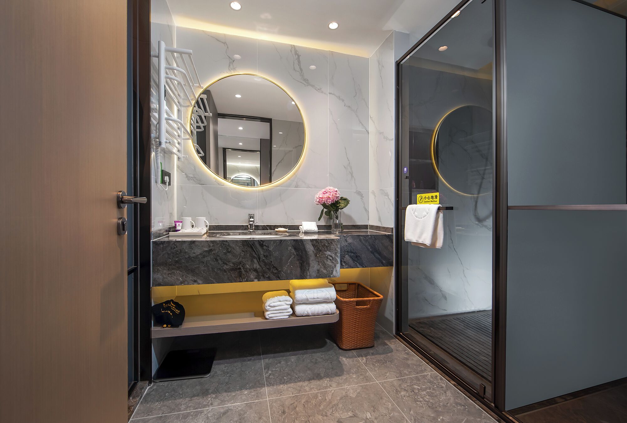 Un baño moderno con lavamanos de mármol, un espejo redondo y una cabina de ducha de vidrio.