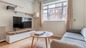 Een moderne woonkamer met een flatscreen televisie, een ronde houten tafel, een grijze bank en een raam met behang.