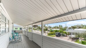 A covered porch with a view of a green house and a boat.