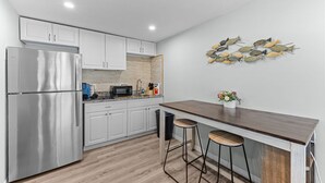 A modern kitchen with white cabinets, a stainless steel refrigerator, a wooden countertop, and a decorative wall art of fish.