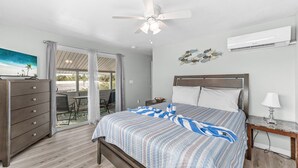 A bedroom with a bed, a dresser, a nightstand, a ceiling fan, and an air conditioning unit.