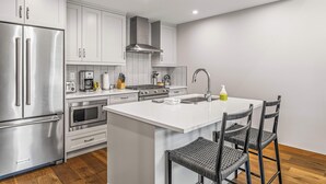 A modern kitchen with stainless steel appliances, a central island with seating, and a bright, minimalist design. - Spring Creek Vacations 1 BR Condo 311TM (Canmore)