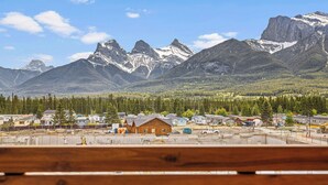 A town with a wooden cabin and houses in the foreground, surrounded by a forest and mountains in the background. - Spring Creek Vacations 1 BR Condo 311TM (Canmore)