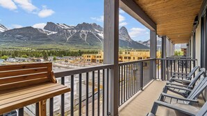 A balcony with a wooden bench and chairs, overlooking a construction site with mountains in the background. - Spring Creek Vacations 1 BR Condo 311TM (Canmore)