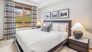 A bedroom with a large bed, two bedside tables with lamps, a ceiling fan, and a window with curtains. - Spring Creek Vacations 2 BR Condo 309TM (Canmore)