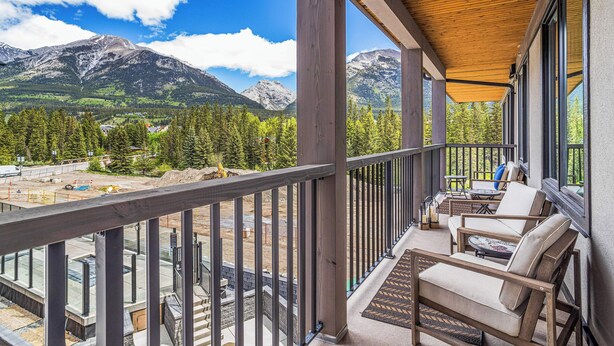 A balcony with a view of mountains, wooden furniture, and a construction site in the background. - Spring Creek Vacations 2 BR Condo 309TM (Canmore)