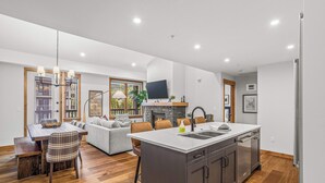 A modern kitchen with a large island, built-in appliances, and a dining area with a fireplace. - Spring Creek Vacations 2 BR Condo 309TM (Canmore)