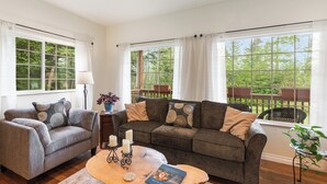 Een woonkamer met twee banken, een salontafel en grote ramen met gordijnen.