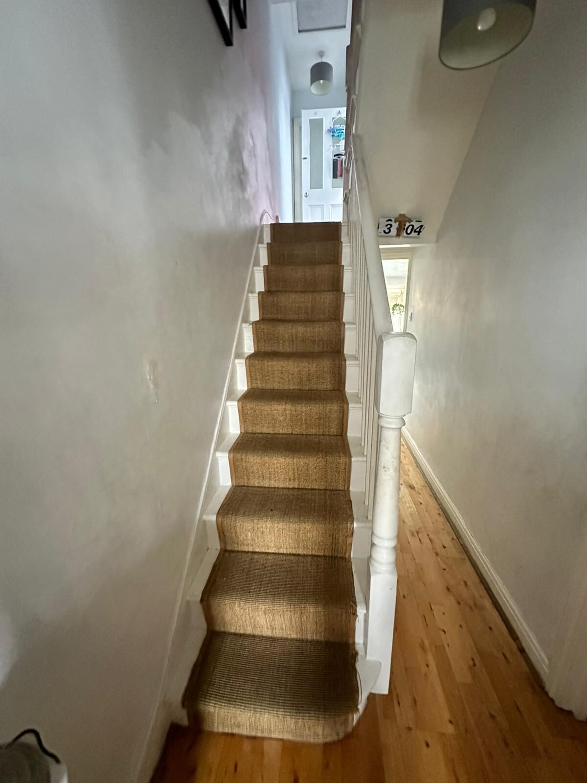 Una escalera con peldaños alfombrados en color beige y barandillas blancas, que conduce a una puerta con el número 304.