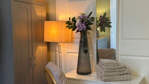 A bathroom with a white vanity, a towel stack, a vase with flowers, and a lamp. - My Sky Secret Garden Near atractions (London)