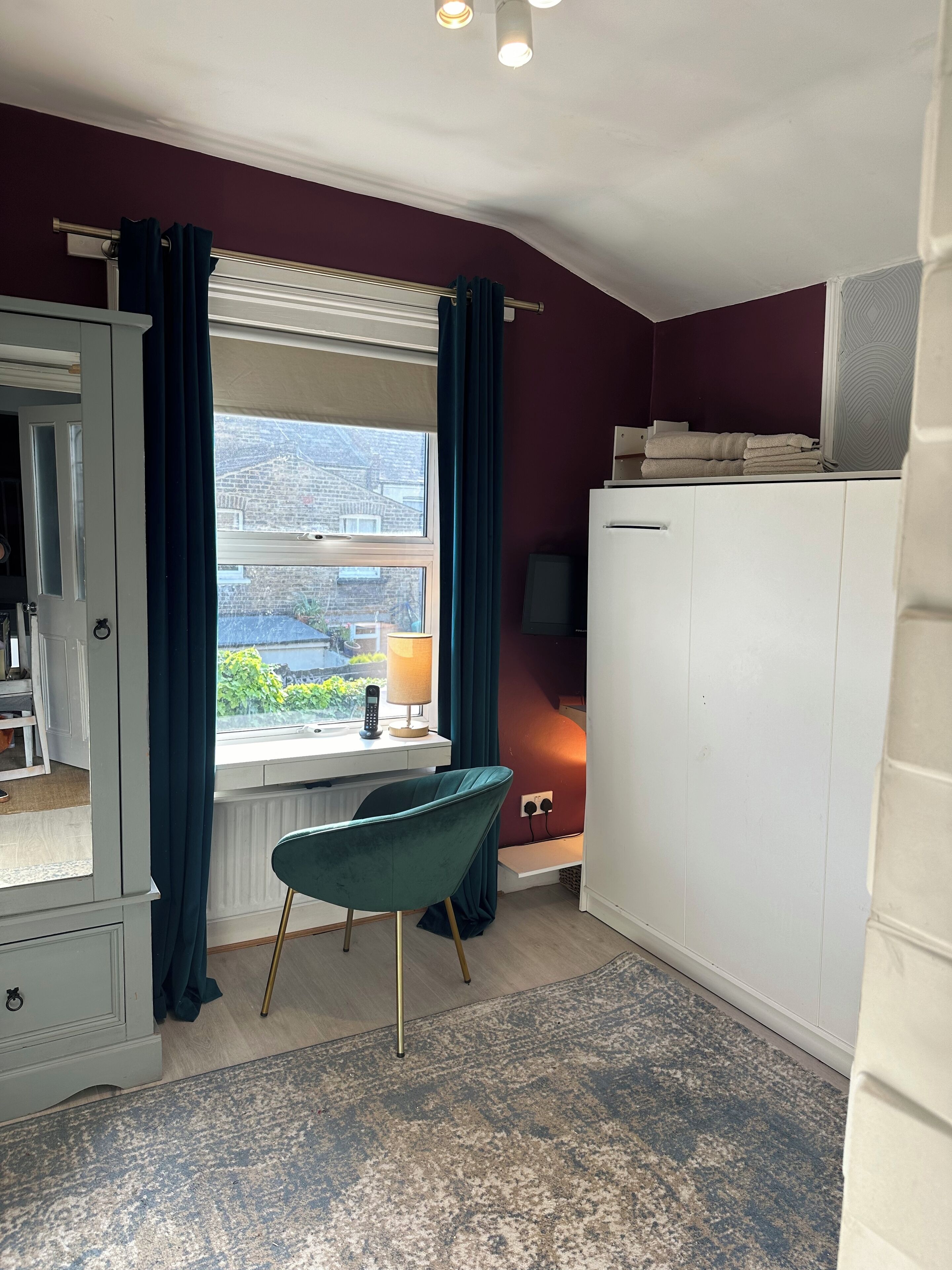 A room with a window, a desk, a chair, a wardrobe, and a radiator.