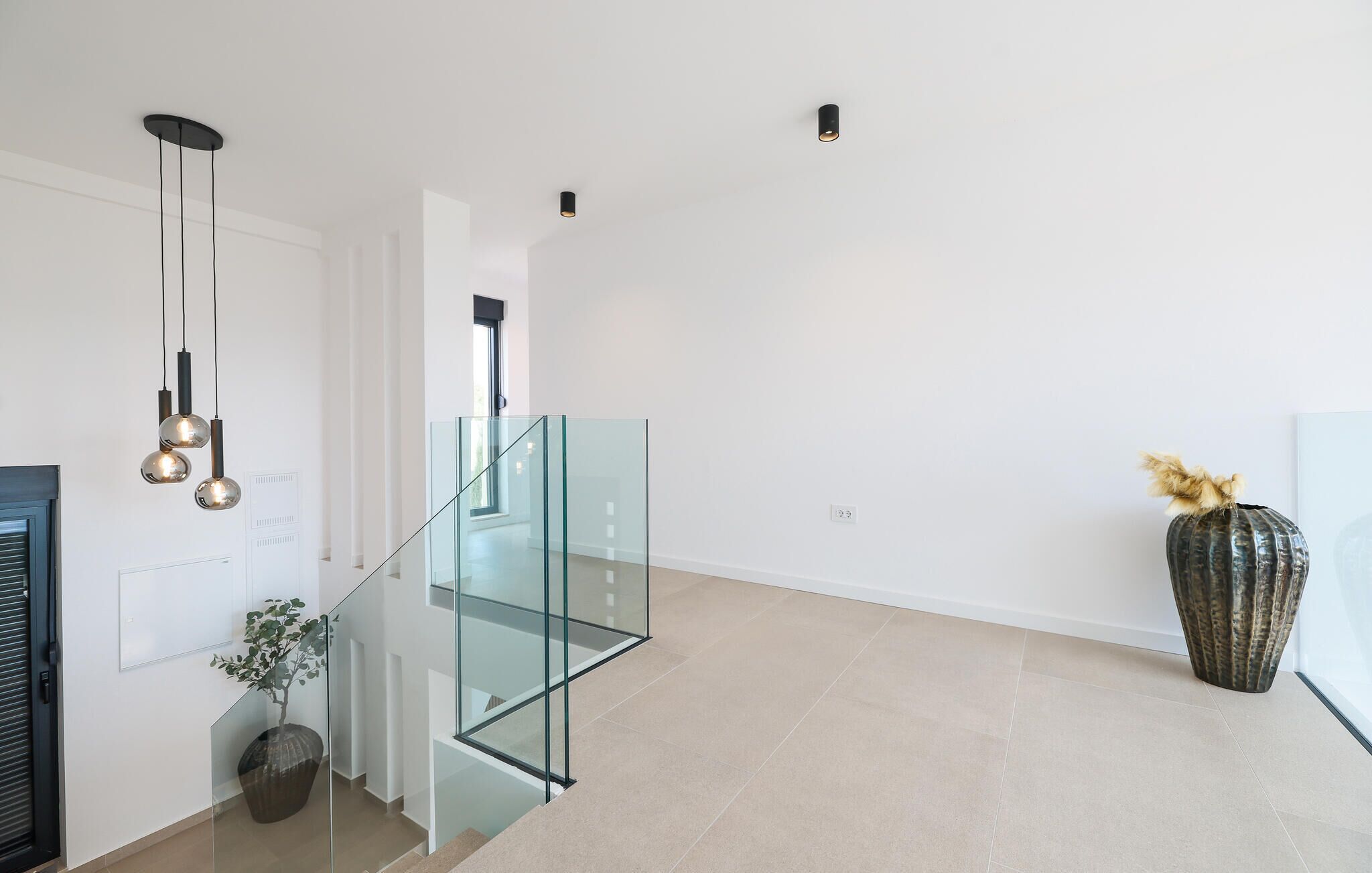 Un interior moderno con una escalera de cristal, decoración minimalista y un jarrón grande.