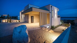 Une maison moderne avec un toit plat, une grande pierre au premier plan et une vue sur la mer en arrière-plan.