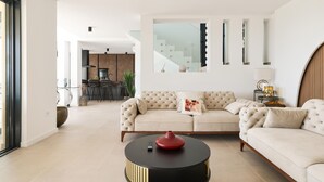 Un salon moderne avec un canapé beige, une table basse ronde et une cuisine en arrière-plan.