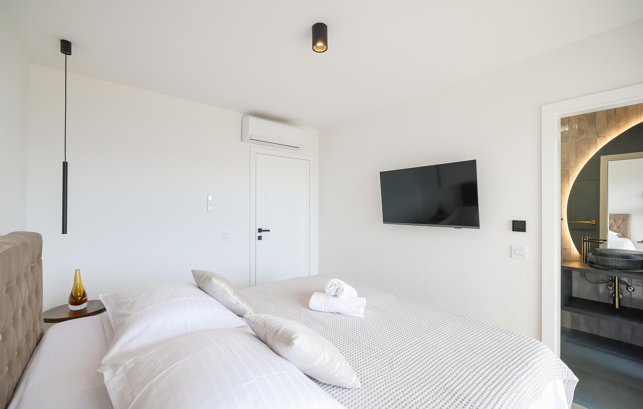 Moderni hotellihuone, jossa on sänky, taulutelevisio, ovi ja kylpyhuone, joka näkyy holvikaaren läpi.