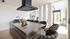 Une cuisine moderne dotée d’un îlot central, de chaises à l’assise rembourrée de couleur foncée et donnant sur un espace extérieur.