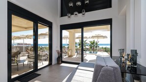 Un salon moderne doté d’une grande porte-fenêtre coulissante donnant sur un balcon aménagé avec du mobilier d’extérieur et des parasols.