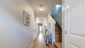 A hallway with wooden flooring, white walls, a staircase with a blue railing, and a small table with a potted plant. - Shared Heated Pool, Golf Cart Access, Pet Friendly (Port Aransas)