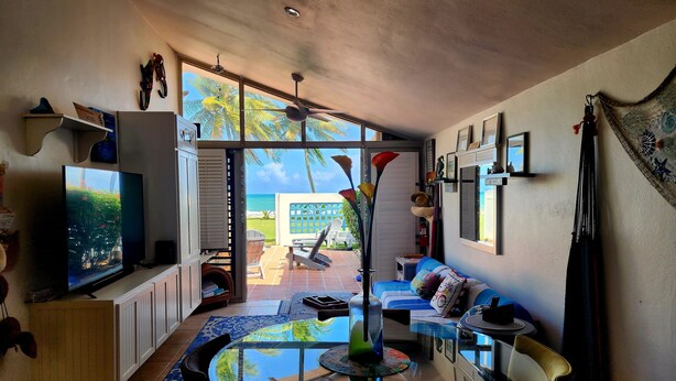 A living room with a glass table, chairs, a sofa, a TV, and a view of the beach. - Ocean Breeze Villa. (Arroyo)
