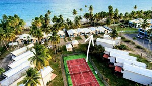An aerial view of a resort with beachside accommodations, a tennis court, and palm trees. - Ocean Breeze Villa. (Arroyo)