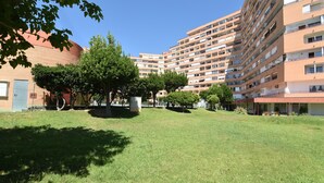 A multi-story residential building with balconies, a grassy courtyard, and trees.