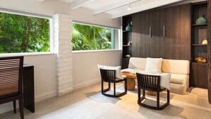 A modern living room with a large window, a white sofa, two wooden chairs, and a dark wooden cabinet with shelves. - Sunrise Bungalow at Largo Resort (Key Largo)