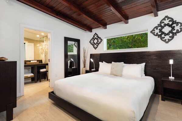 A bedroom with a large bed, a nightstand, a dresser, a mirror, and a wall-mounted artwork. - Enchanted Paradise Bungalow at Largo Resort (Key Largo)