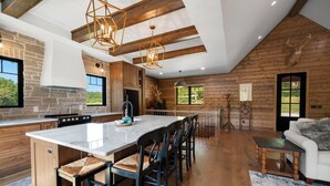 A spacious kitchen with a large island, wooden beams, and a stone wall. - Cedar Cove Cabin, Private Beach near Galena (Elizabeth)