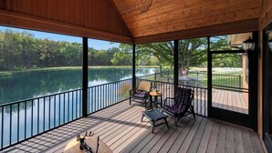 A covered deck with a view of a lake, furnished with chairs and a table, and a hanging light fixture. - Cedar Cove Cabin, Private Beach near Galena (Elizabeth)