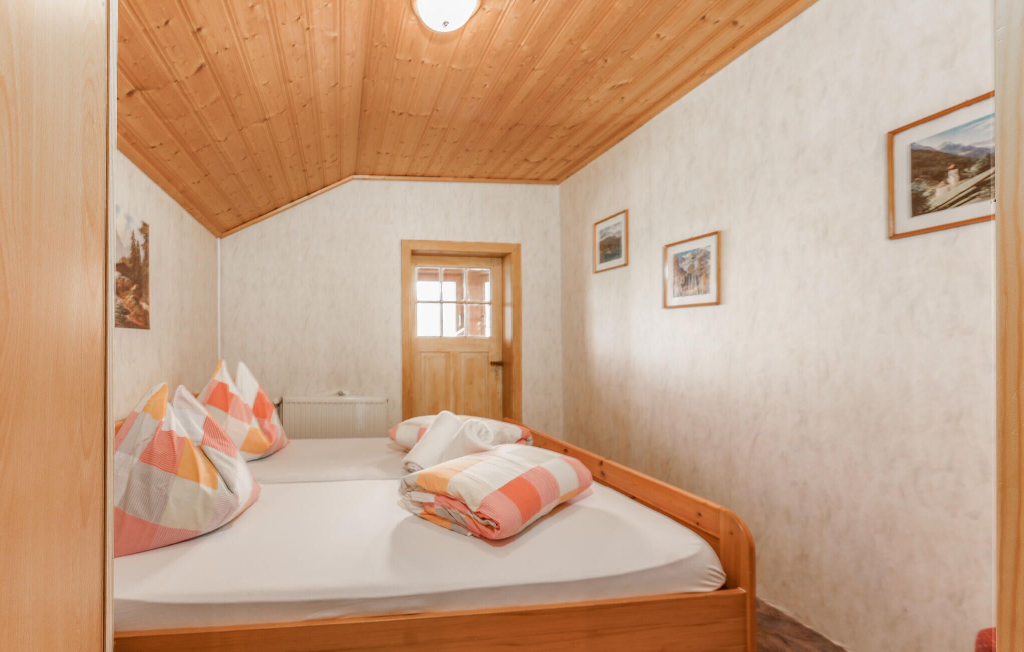 A bedroom with two beds, a wooden ceiling, a radiator, and framed pictures on the walls.