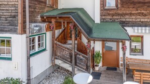 Un edificio de madera tradicional con una escalera de techo verde, un banco de madera y una puerta con una planta en maceta a un lado.