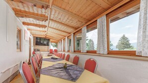 Un salón de conferencias con una larga mesa, sillas rojas y amplias ventanas que dan a vistas de árboles y montañas.
