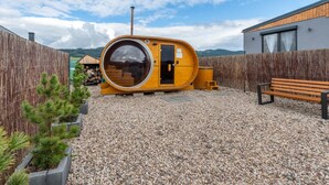Una sauna de madera con puerta circular, banco de madera y suelo de grava.