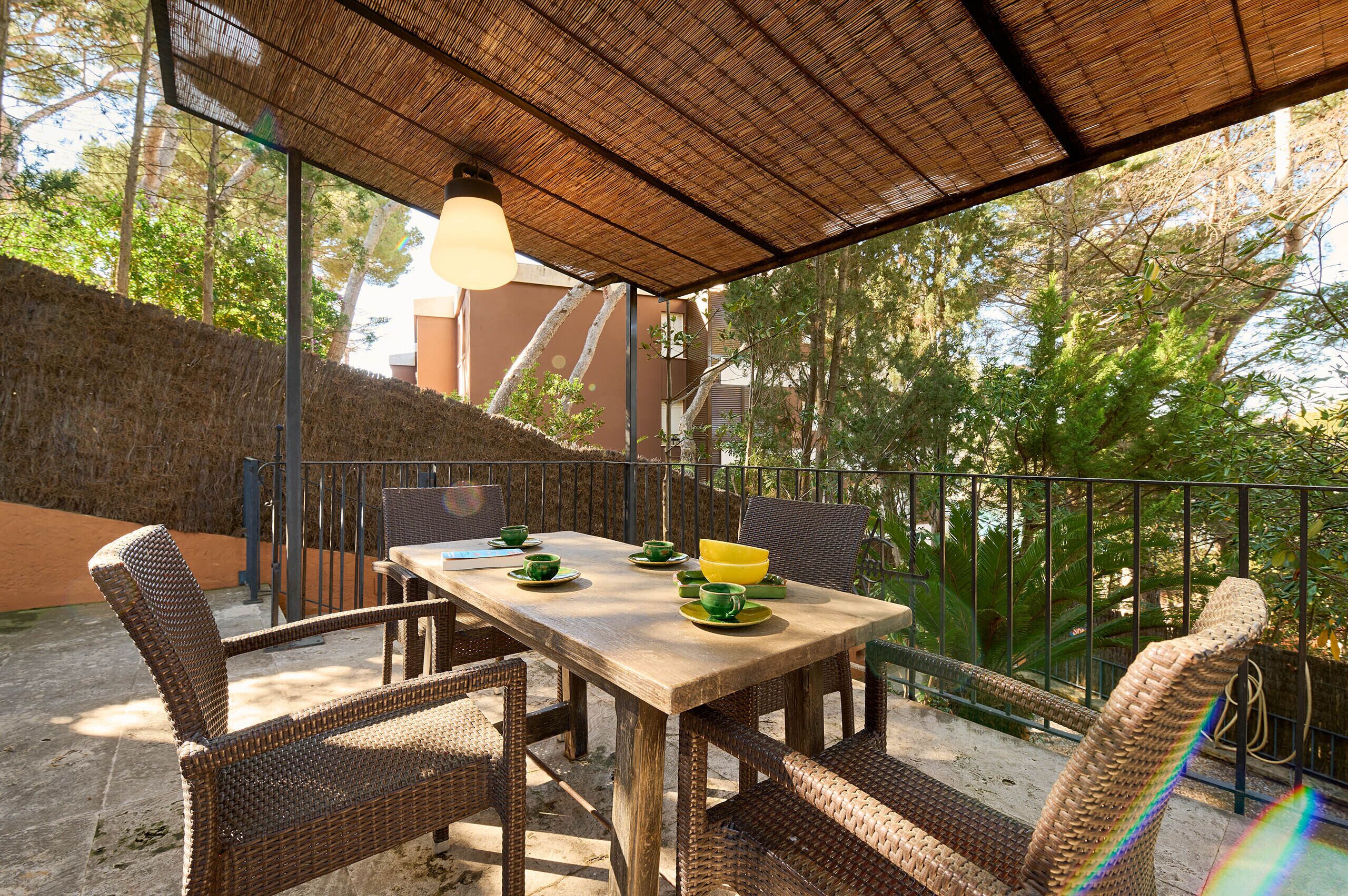 An outdoor patio with a wooden table and wicker chairs, surrounded by a metal railing and a bamboo roof.