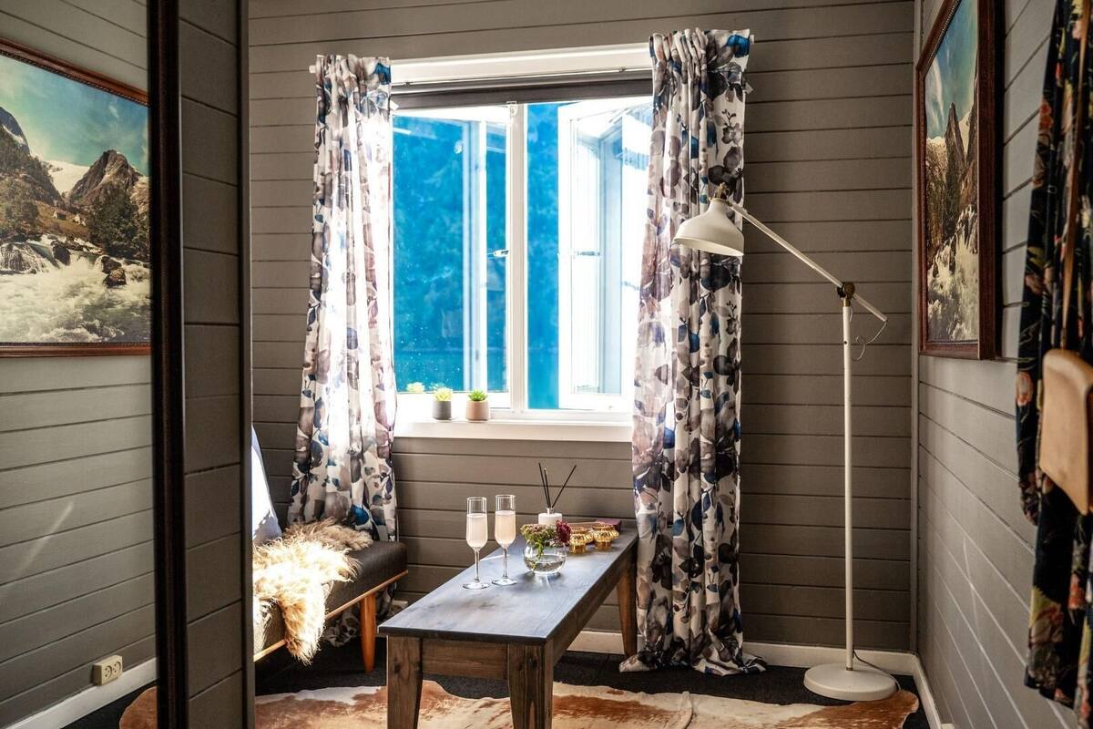 Ein gemütliches Zimmer mit Fenster, Tisch mit Gläsern und Kerze, sowie einer Stehlampe.
