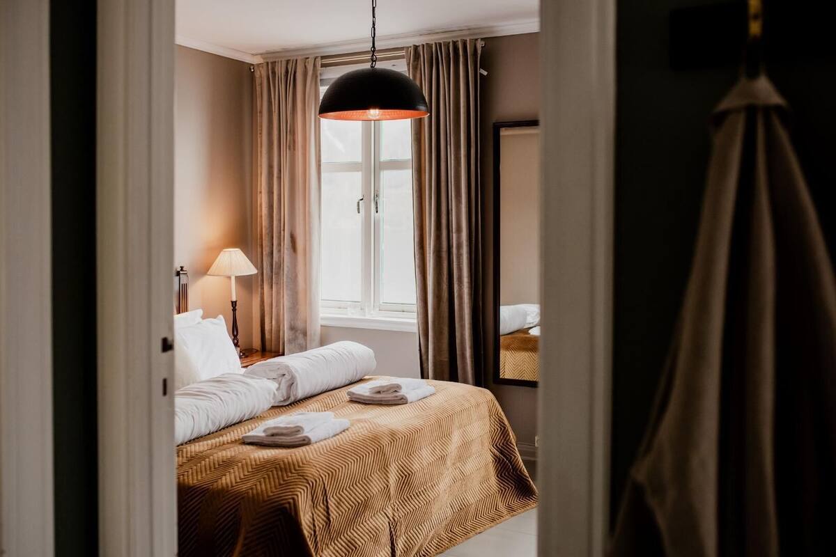 Ein Hotelzimmer mit Bett, Lampe, einem Fenster mit Vorhängen und einer Pendelleuchte.