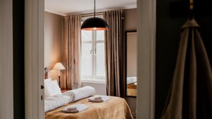 Una habitación de hotel con cama, lámpara, ventana con cortinas y lámpara colgante.
