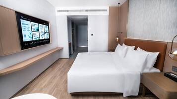 A modern hotel room with a large bed, a mounted TV displaying content, a bedside table, and a nightstand.