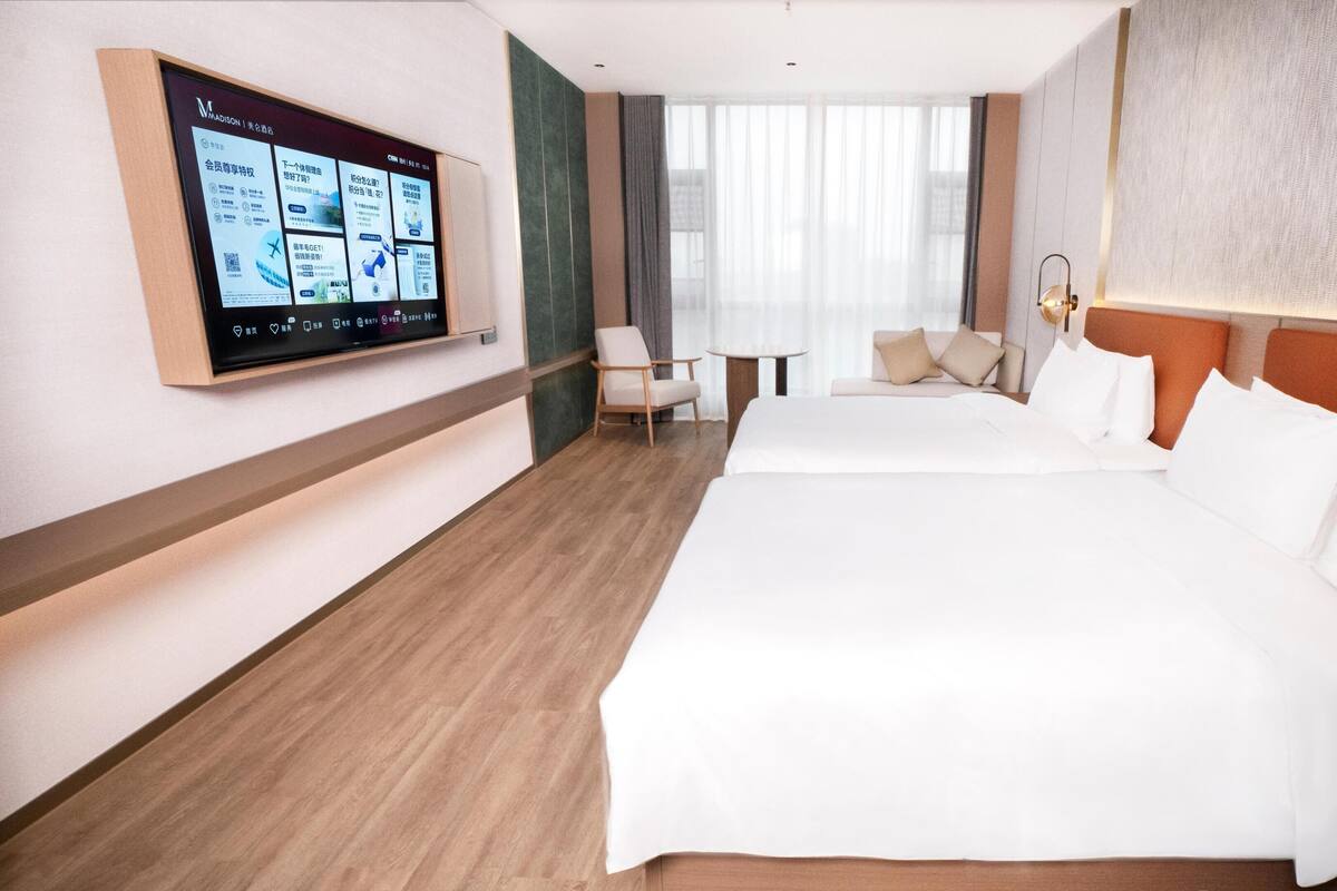 Ein Hotelzimmer mit einem großen Bett, einem Schreibtisch, einem Sessel und einem an der Wand montierten Fernseher.